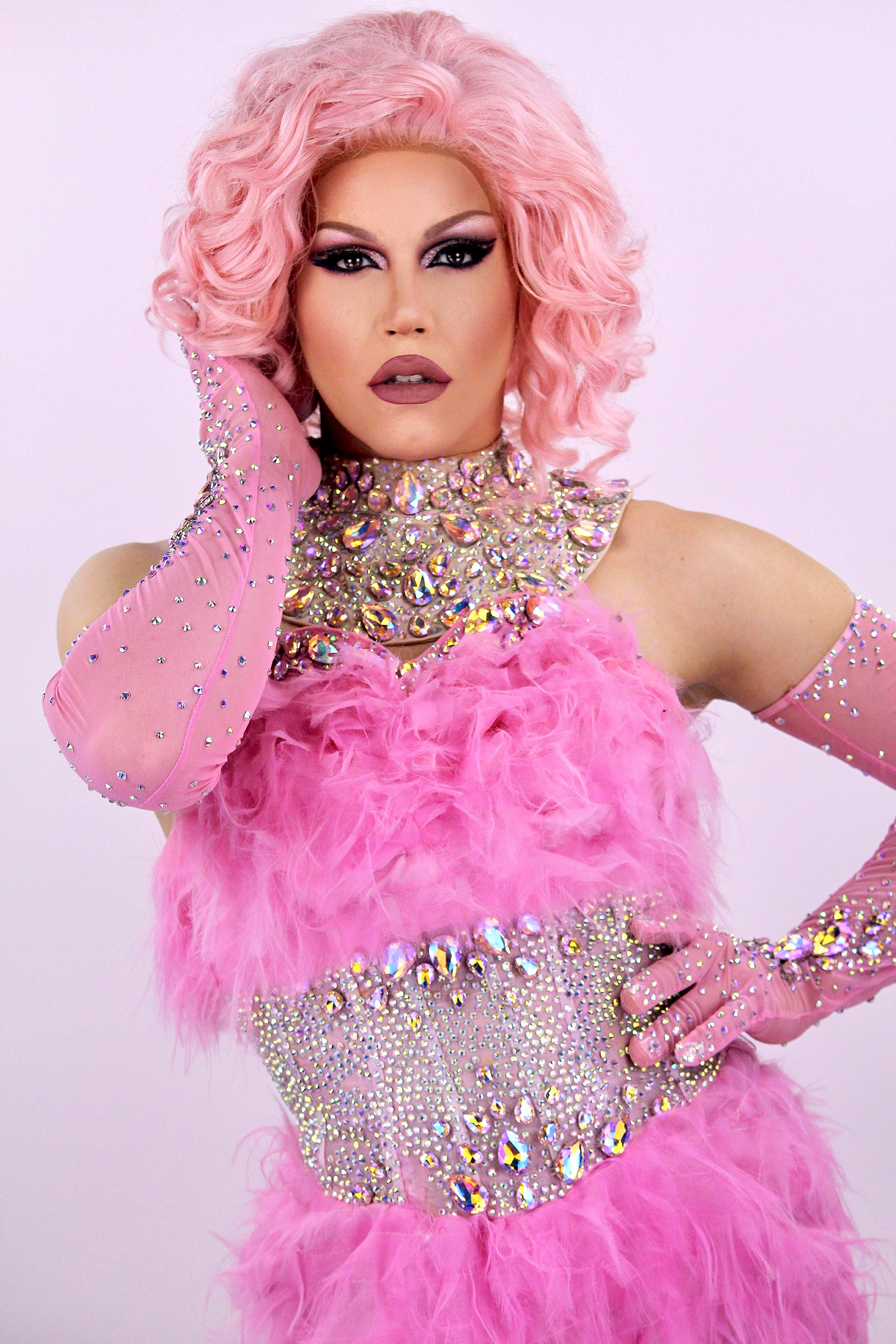 Photo d'une artiste drag queen de l'agence NA Events avec des cheveux roses, portant une robe rose à plumes et strass, idéale pour l'animation mariage et d'événements privés.