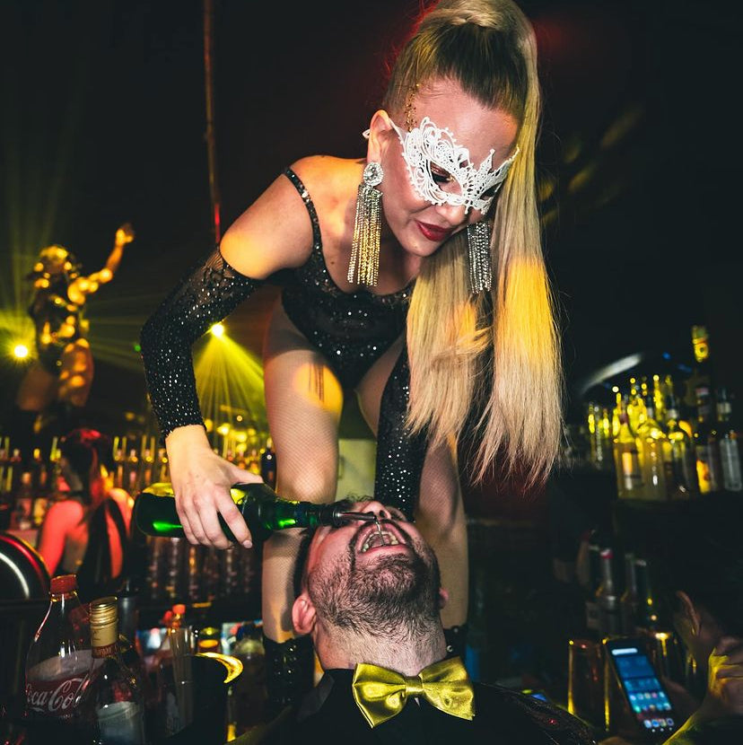 Une artiste gogo de l'agence NA Events dans une boîte de nuit en tenue strass avec un masque type loup vénitien, qui sert à boire à un client pour une ambiance de folie.