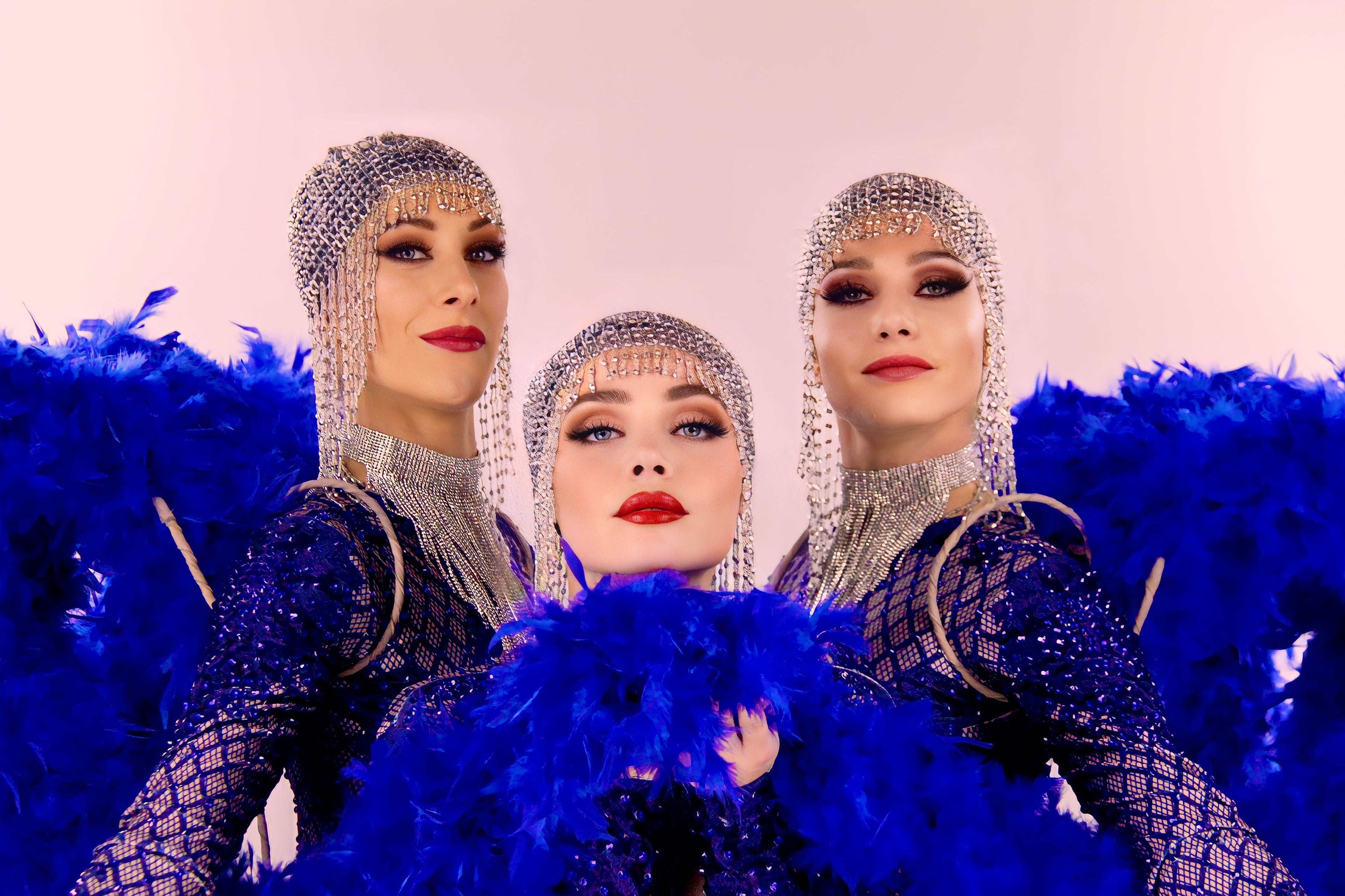Trois danseuses de cabaret de l'agence NA Events, portant des tenues à strass et de grandes plumes bleues lors d'un spectacle.