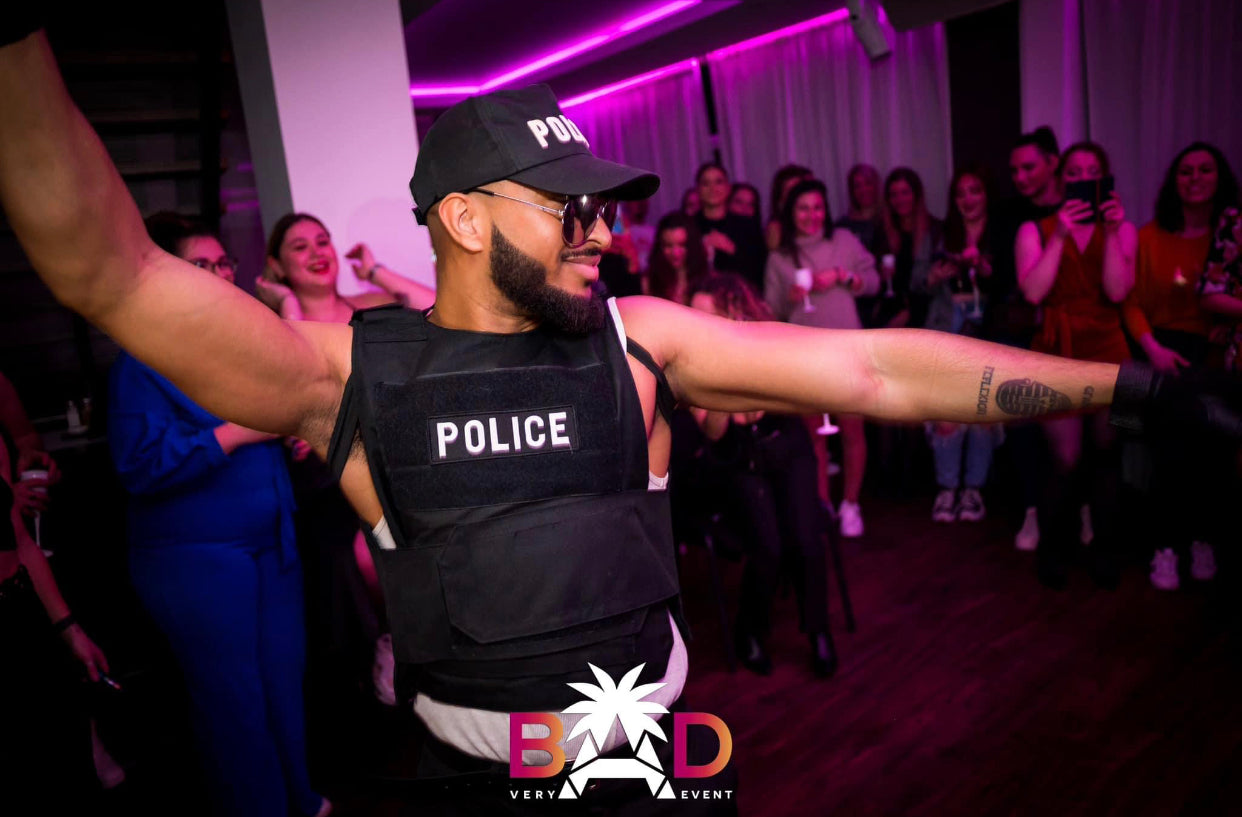 Un artiste stripteaseur de l'agence NA Events en tenue de policier, dansant sur la piste entouré de clients lors d'un événement privé à domicile. 